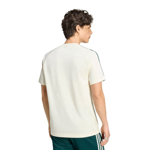 A man seen from the back wearing an adidas Real Madrid Originals T-Shirt, a cream-colored, short-sleeved shirt with green stripes along the sleeves.