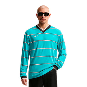 A man wears a teal Nike Energy Long Sleeve T-Shirt featuring horizontal white stripes, black sleeve cuffs, and a black collar as part of his official soccer gear.
