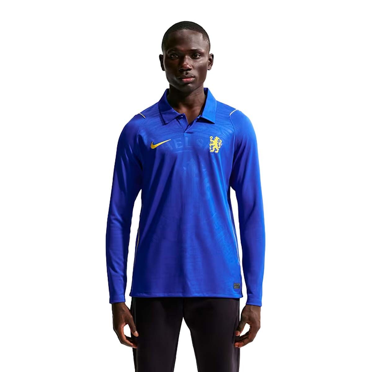 A man wearing a Nike Chelsea FC 26/27 Long Sleeve Stadium Home Jersey with a collar, featuring a yellow logo on the chest and a crest on the opposite side.
