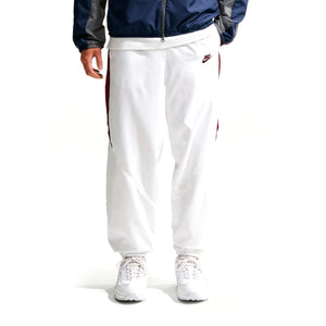 Nike Premier Repel white athletic pants with dark vertical side stripes and a small logo on the left hip, worn with a dark blue jacket and white sneakers for an official soccer gear look.