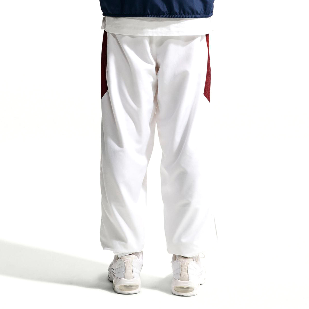 Back view of Nike Premier Repel Pants, featuring white athletic fabric with dark red side panels, worn with white sneakers as official soccer gear.