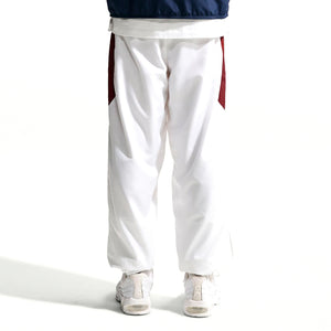 Back view of Nike Premier Repel Pants, featuring white athletic fabric with dark red side panels, worn with white sneakers as official soccer gear.