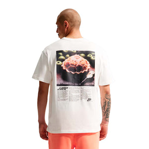 A person wears a white Nike Sportswear T-Shirt featuring a large graphic of an apple pie on the back with the text As American as apple pie, perfect for soccer gear enthusiasts.