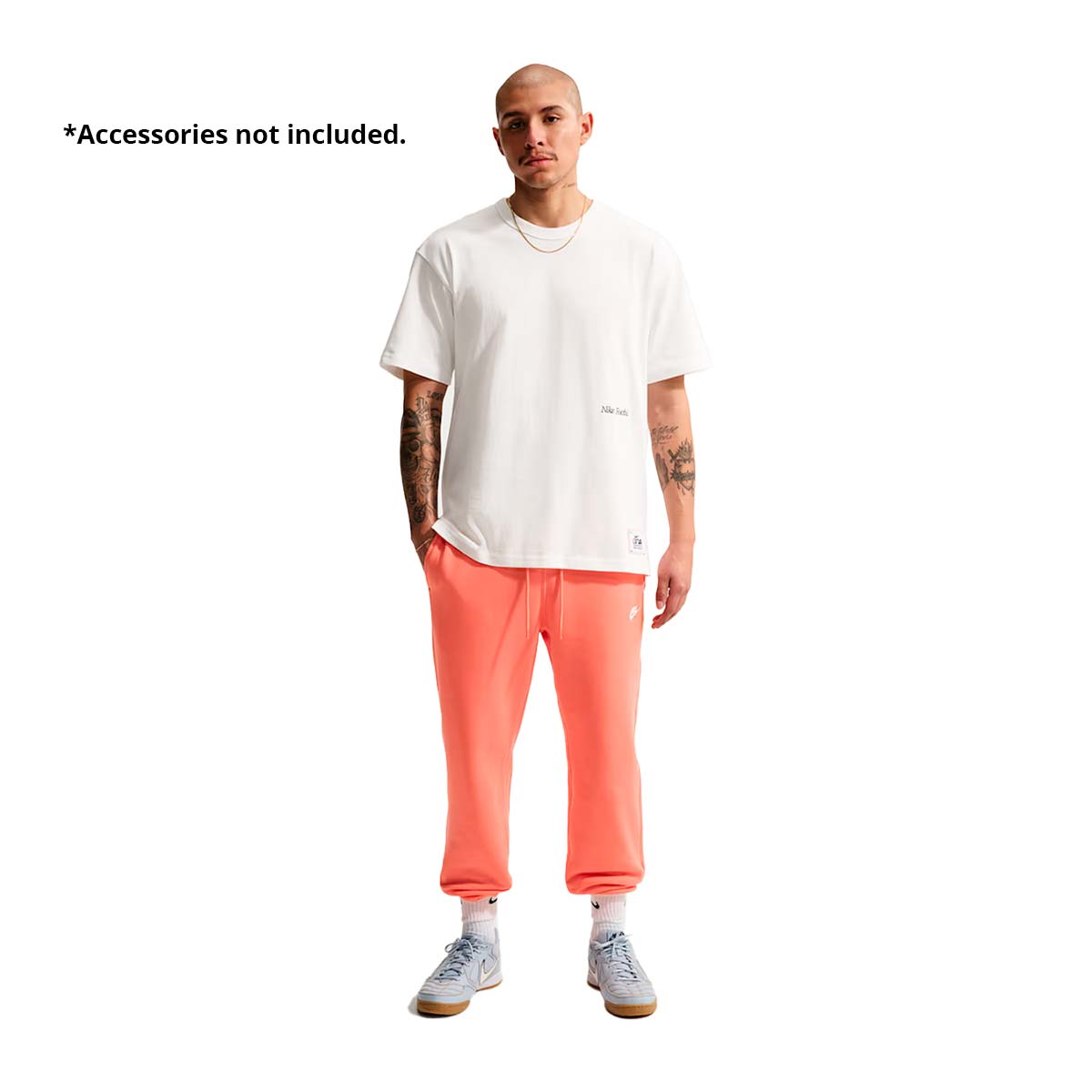 A man wears a white Nike Sportswear T-Shirt and coral-colored sweatpants as part of his game-day look.