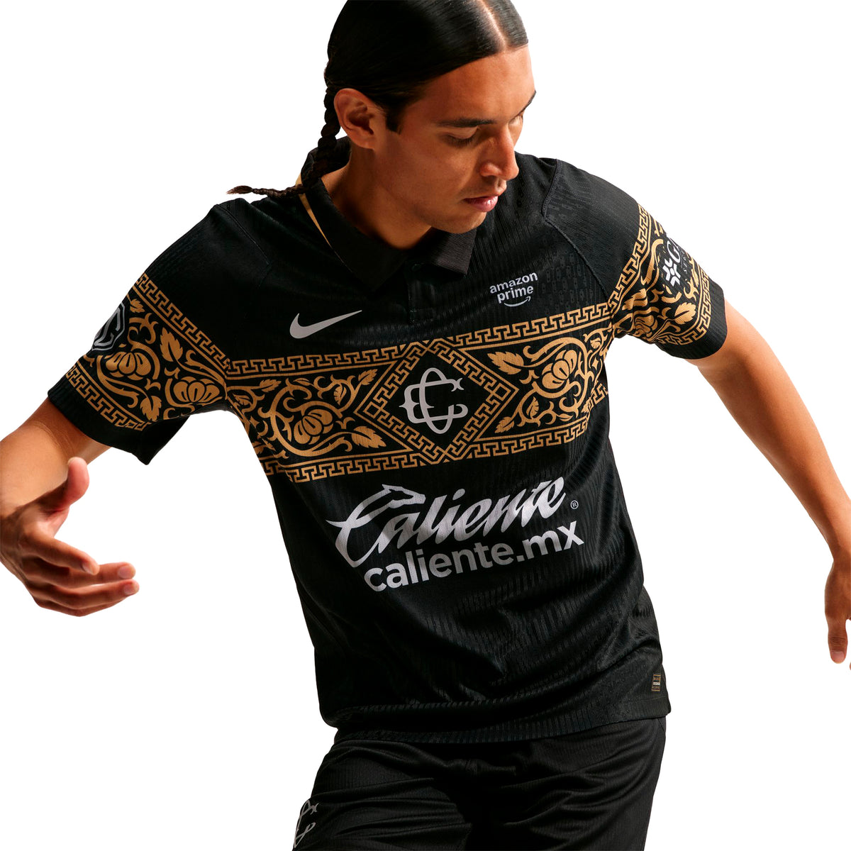 A person wears a black Nike Chivas 26/27 Match Third Autenthic Jersey featuring gold floral and geometric patterns across the chest, accented by a white logo and sponsor text.