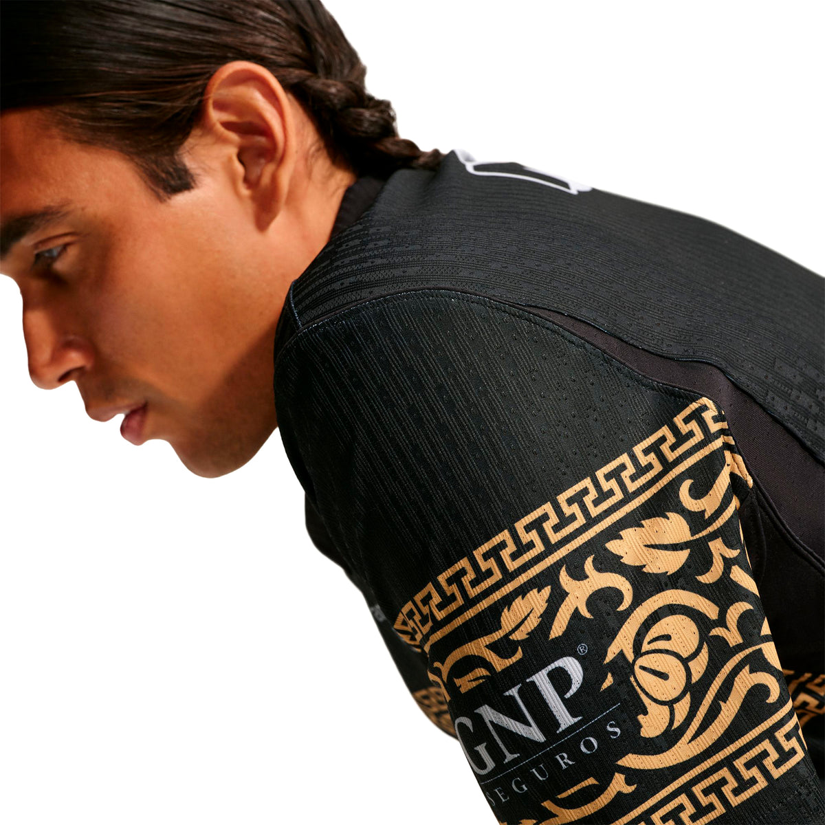 A person wearing a black Nike Chivas 26/27 Match Third Autenthic Jersey featuring a gold Greek key pattern on the shoulder and a gold logo on the sleeve.