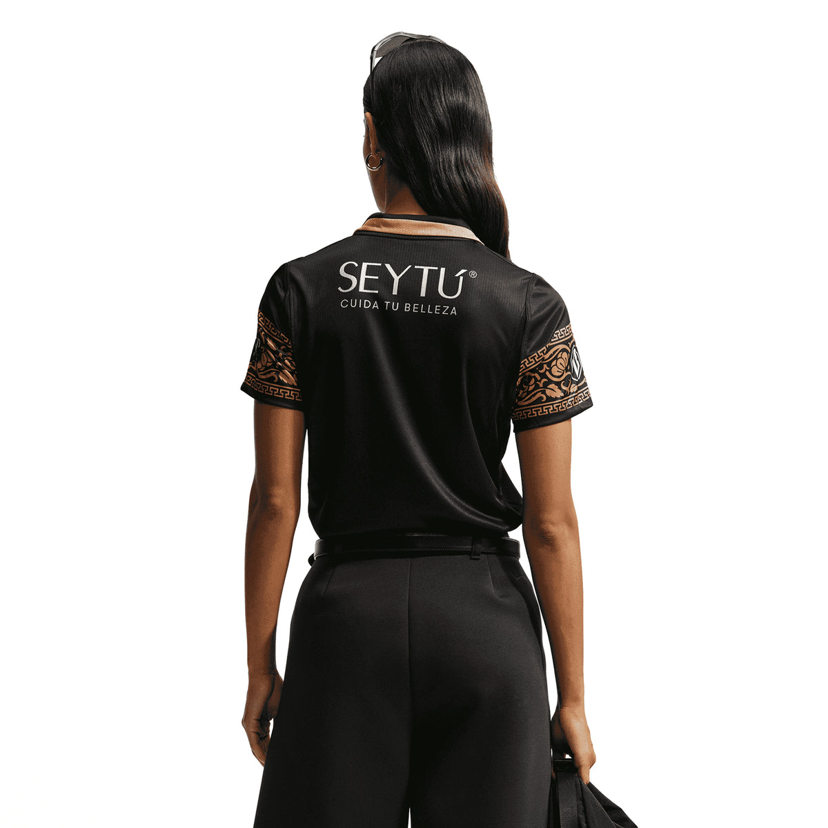A person seen from behind wearing a black Nike Chivas 26/27 Stadium Third Jersey with a tan collar, patterned sleeves, and SEYTÚ CUIDA TU BELLEZA printed in white on the back.