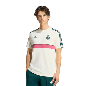 An off-white adidas Real Madrid Originals T-Shirt featuring a teal trefoil logo, a Real Madrid crest, a horizontal pink stripe across the chest, and teal shoulder stripes.